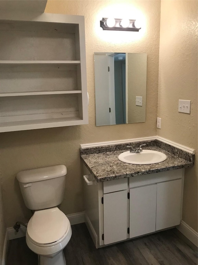 half bathroom with baseboards, toilet, wood finished floors, and vanity