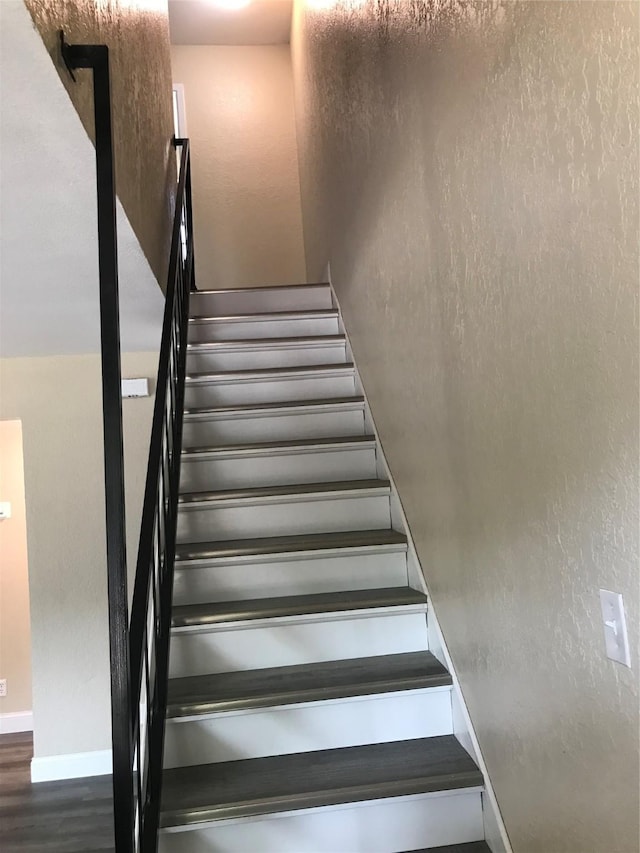 staircase with a textured wall, baseboards, and wood finished floors