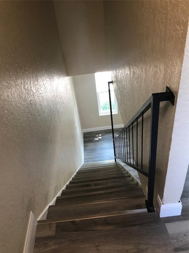 stairway featuring baseboards, a textured wall, and wood finished floors