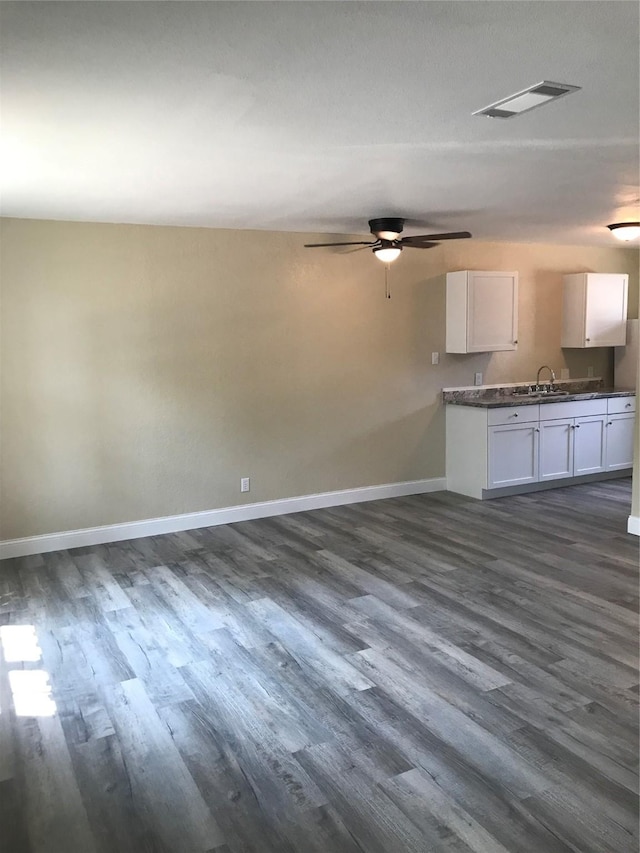 unfurnished living room featuring a ceiling fan, baseboards, visible vents, dark wood finished floors, and a sink