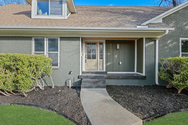 doorway to property featuring brick siding and a shingled roof