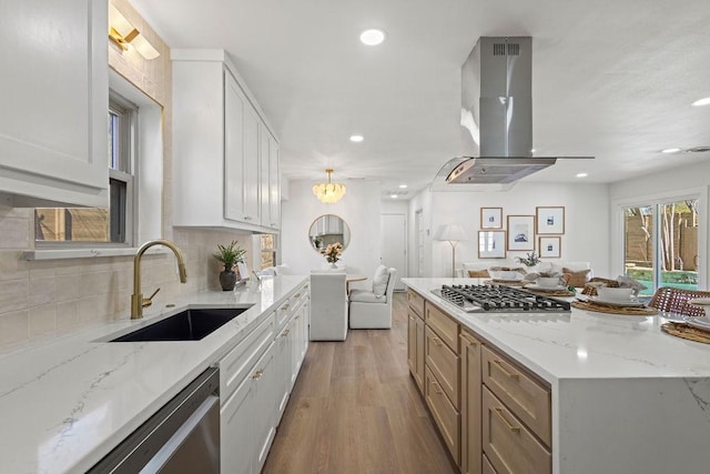 kitchen with open floor plan, range hood, appliances with stainless steel finishes, light wood-style floors, and a sink