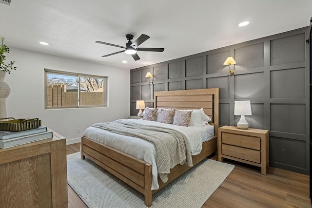 bedroom featuring a ceiling fan, a decorative wall, recessed lighting, and wood finished floors