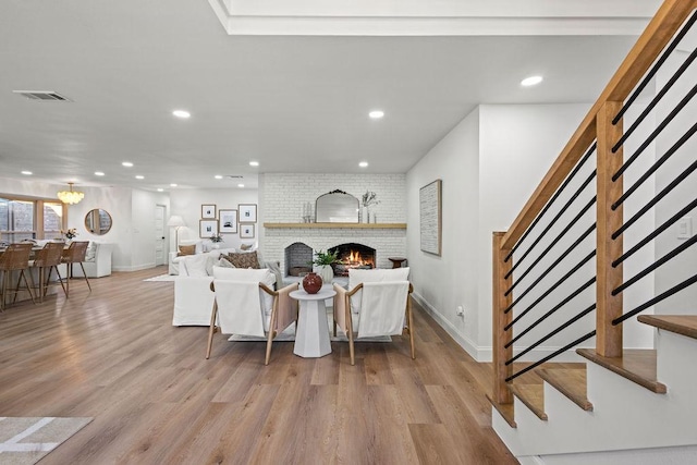 living room with stairway, a brick fireplace, visible vents, and wood finished floors