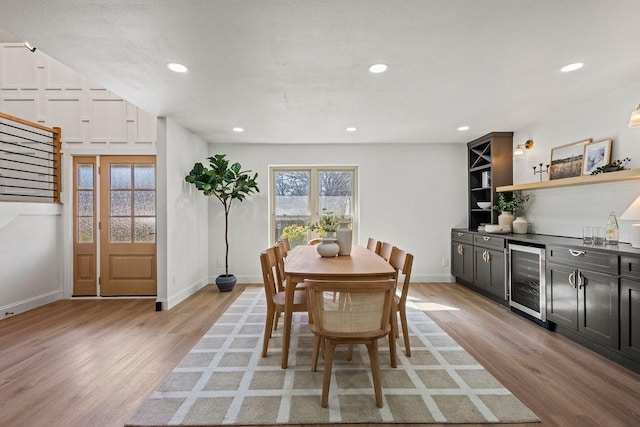 dining space with a bar, light wood-style flooring, beverage cooler, and baseboards