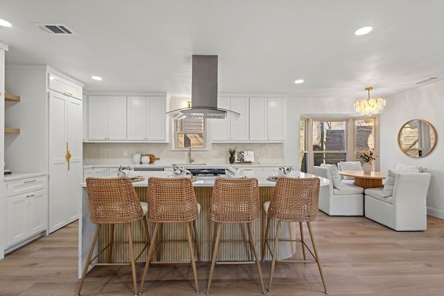 kitchen featuring light wood finished floors, visible vents, light countertops, island range hood, and white cabinets