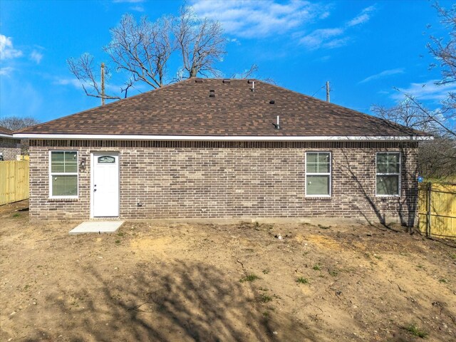 rear view of property featuring brick siding, roof with shingles, and fence