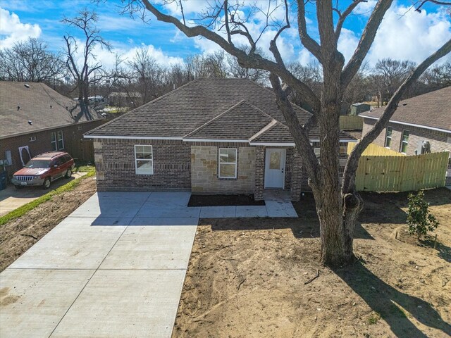 view of front of property featuring brick siding, fence, stone siding, and roof with shingles