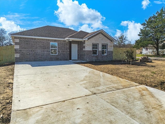 ranch-style home featuring fence, a shingled roof, concrete driveway, stone siding, and brick siding