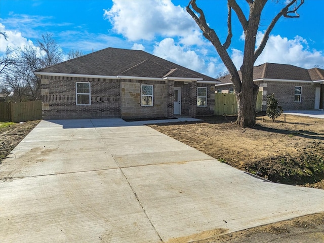 ranch-style home featuring fence, brick siding, and a shingled roof