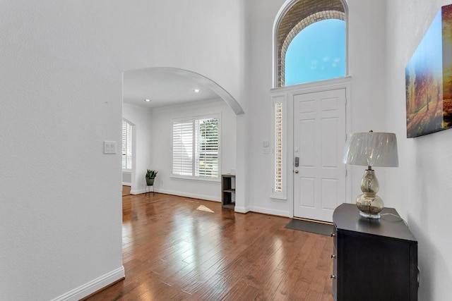 entryway featuring baseboards, recessed lighting, a high ceiling, wood finished floors, and arched walkways