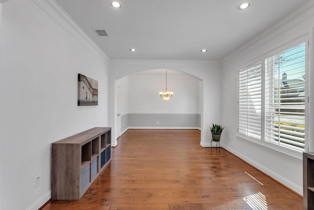 unfurnished living room featuring arched walkways, visible vents, ornamental molding, and wood finished floors