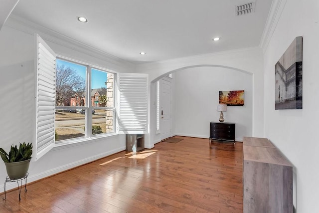 unfurnished living room with visible vents, crown molding, baseboards, wood finished floors, and arched walkways