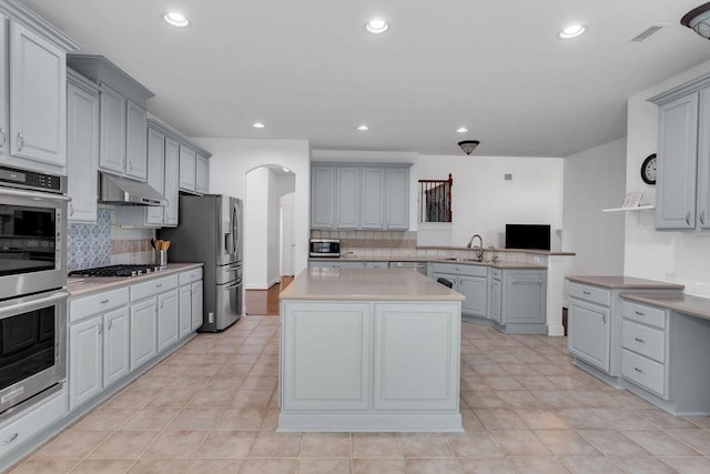 kitchen with under cabinet range hood, gray cabinetry, stainless steel appliances, and arched walkways