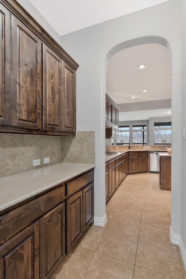 kitchen featuring dark brown cabinets, dishwasher, decorative backsplash, light tile patterned flooring, and arched walkways