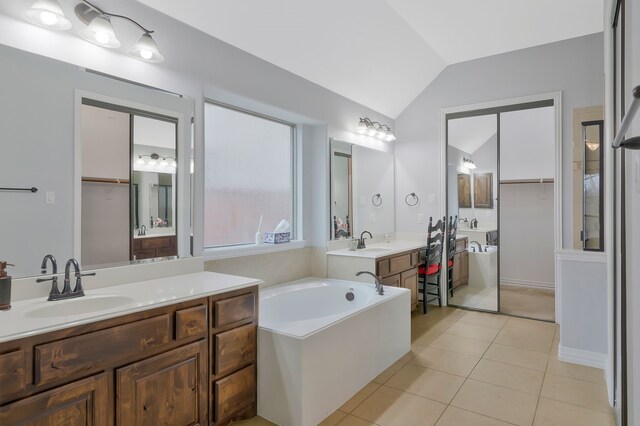 bathroom featuring tile patterned floors, a garden tub, two vanities, a sink, and vaulted ceiling