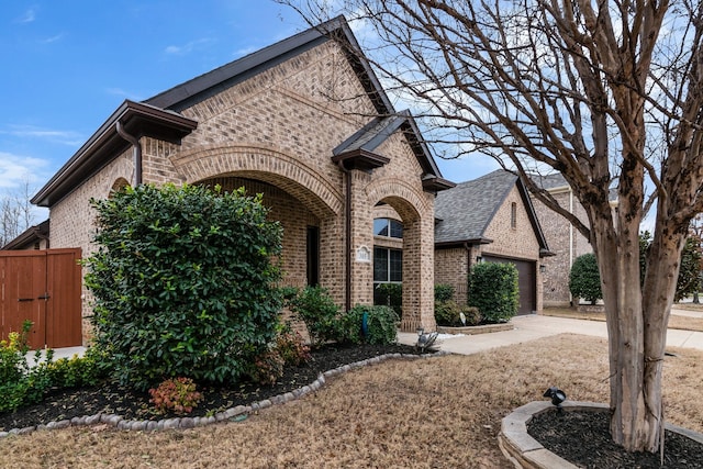 french country inspired facade featuring concrete driveway, an attached garage, fence, and brick siding