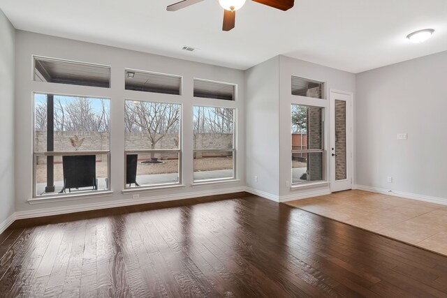 unfurnished living room featuring wood finished floors, visible vents, a wealth of natural light, and baseboards