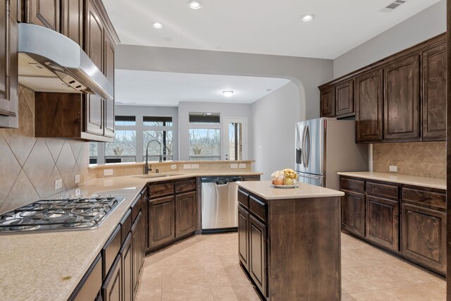 kitchen featuring ventilation hood, arched walkways, a sink, light countertops, and appliances with stainless steel finishes