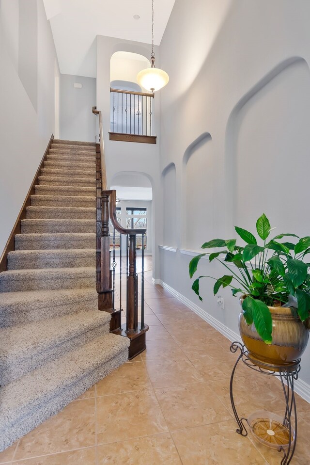 staircase featuring tile patterned flooring, baseboards, and a towering ceiling