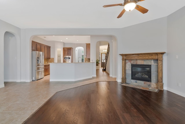 unfurnished living room featuring ceiling fan, baseboards, a tiled fireplace, light wood-style floors, and a sink