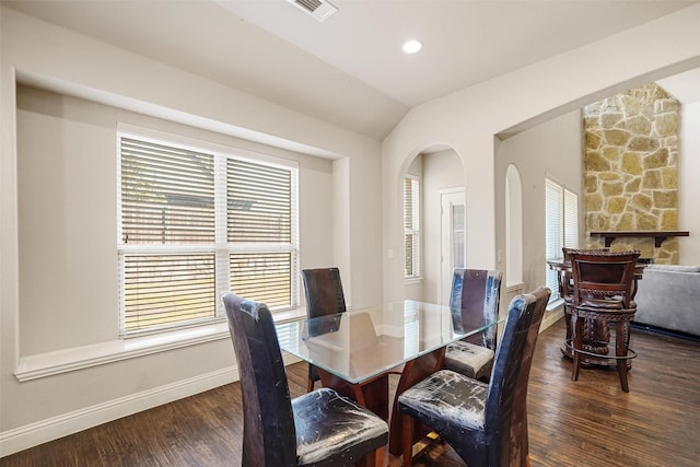 dining space with visible vents, wood finished floors, arched walkways, baseboards, and vaulted ceiling