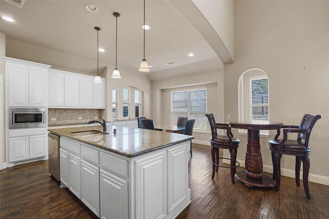 kitchen with dark wood-type flooring, a center island with sink, a sink, arched walkways, and appliances with stainless steel finishes