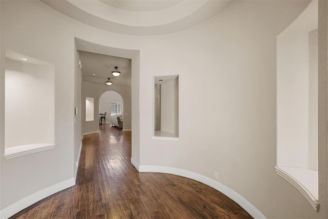 corridor with arched walkways, dark wood-type flooring, and baseboards