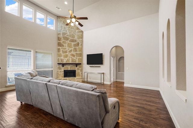 living area featuring a stone fireplace, arched walkways, visible vents, and dark wood-style flooring