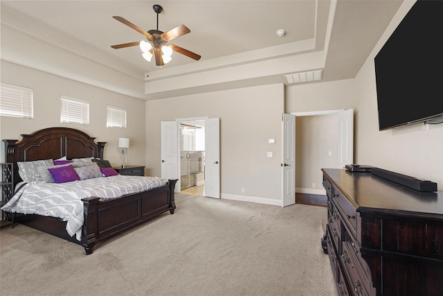 bedroom featuring visible vents, baseboards, light carpet, ensuite bath, and a raised ceiling