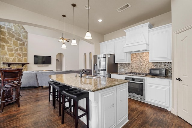 kitchen featuring visible vents, custom exhaust hood, arched walkways, decorative backsplash, and appliances with stainless steel finishes