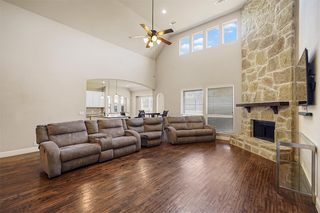 living room with a stone fireplace, visible vents, wood finished floors, and arched walkways