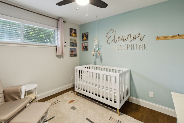 bedroom featuring baseboards, a ceiling fan, a nursery area, and wood finished floors