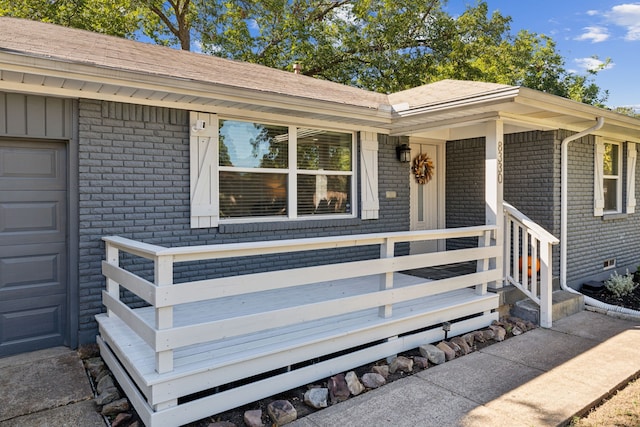 doorway to property featuring board and batten siding, a porch, a garage, and brick siding