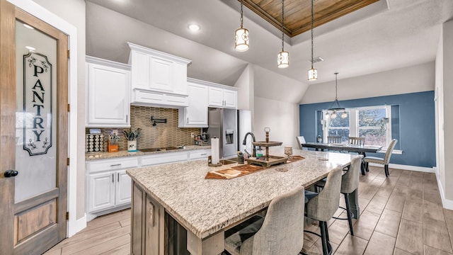 kitchen with backsplash, wood finish floors, a center island with sink, stainless steel refrigerator with ice dispenser, and a raised ceiling