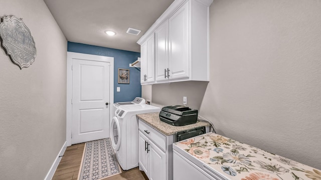 clothes washing area featuring visible vents, light wood-style flooring, washing machine and dryer, cabinet space, and baseboards