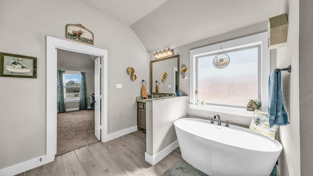 full bathroom with vanity, wood finished floors, baseboards, a soaking tub, and lofted ceiling