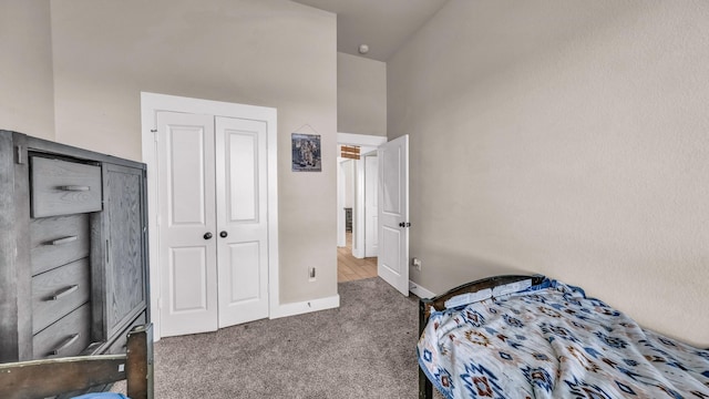 carpeted bedroom featuring a high ceiling, baseboards, and a closet