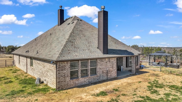 back of property featuring a gazebo, brick siding, roof with shingles, and fence