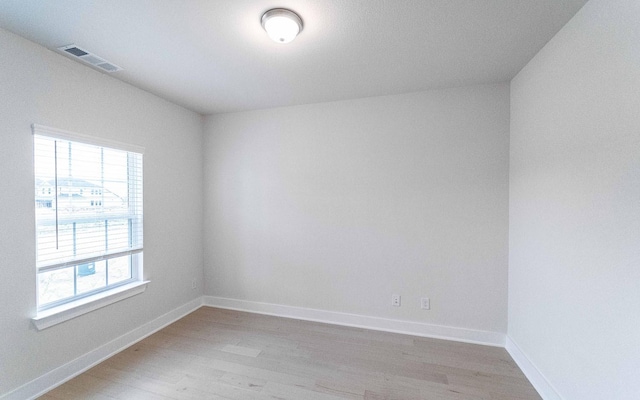 empty room with baseboards, visible vents, and light wood finished floors