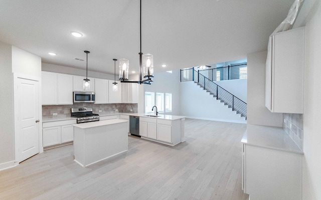 kitchen with light countertops, appliances with stainless steel finishes, a peninsula, light wood-style floors, and a sink