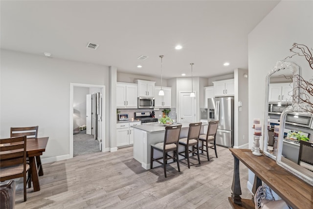 kitchen featuring a kitchen bar, visible vents, a center island with sink, light wood-style flooring, and stainless steel appliances