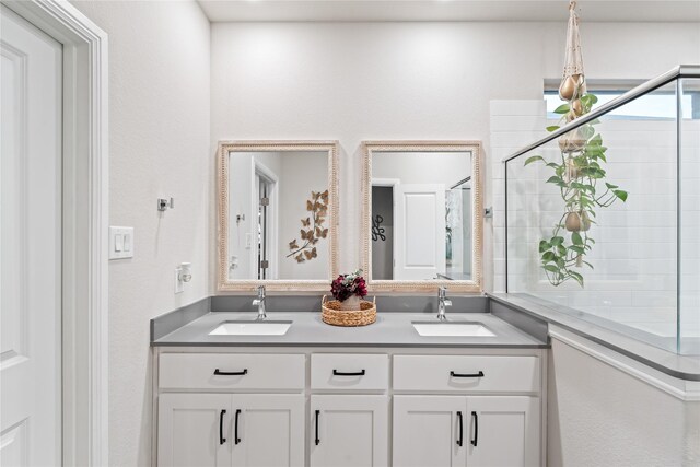 full bathroom featuring double vanity, tiled shower, and a sink