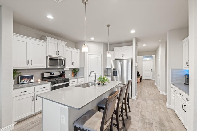 kitchen featuring backsplash, a kitchen bar, light wood-style flooring, appliances with stainless steel finishes, and a sink