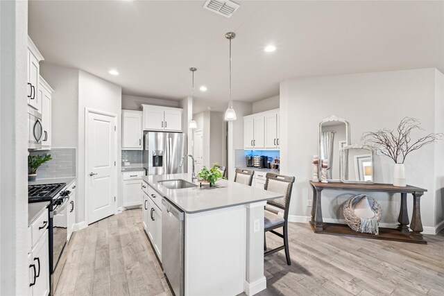 kitchen featuring visible vents, light wood-style flooring, a sink, stainless steel appliances, and a kitchen bar