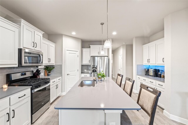 kitchen featuring a center island with sink, light wood-style flooring, a sink, appliances with stainless steel finishes, and white cabinetry