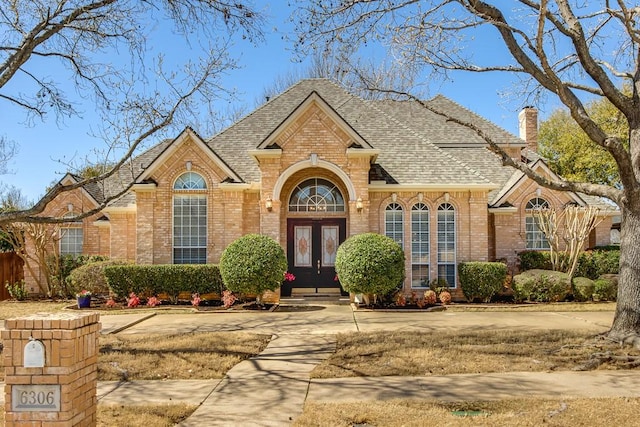 traditional-style house with brick siding, french doors, and a shingled roof