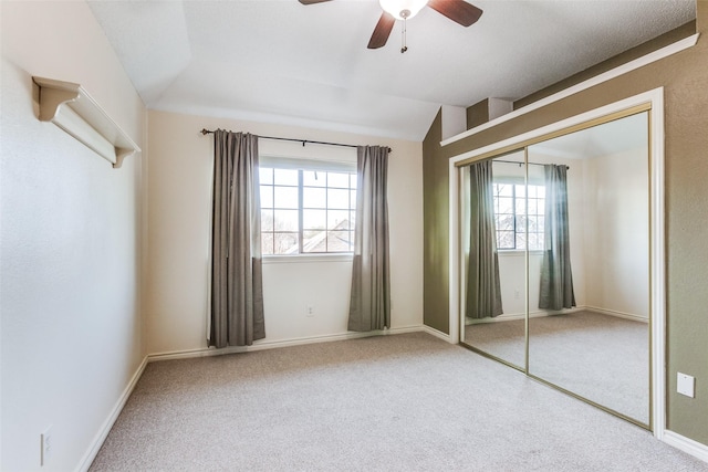 unfurnished bedroom with baseboards, carpet, lofted ceiling, a closet, and a ceiling fan