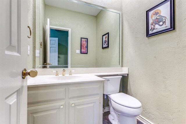 bathroom with toilet, vanity, baseboards, and a textured wall