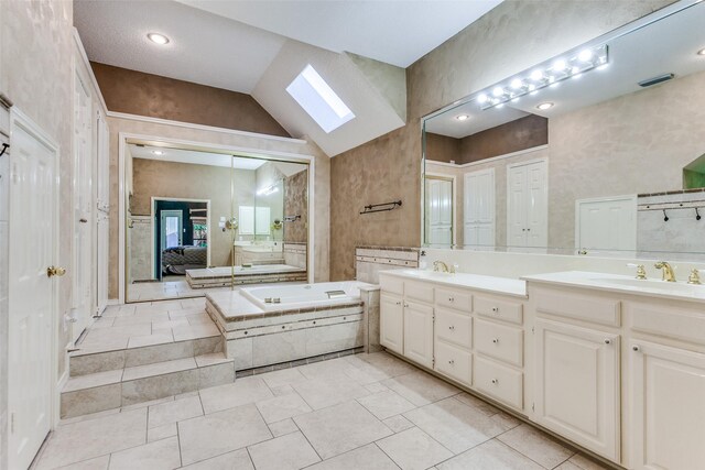 ensuite bathroom featuring lofted ceiling with skylight, visible vents, a bath, and a sink